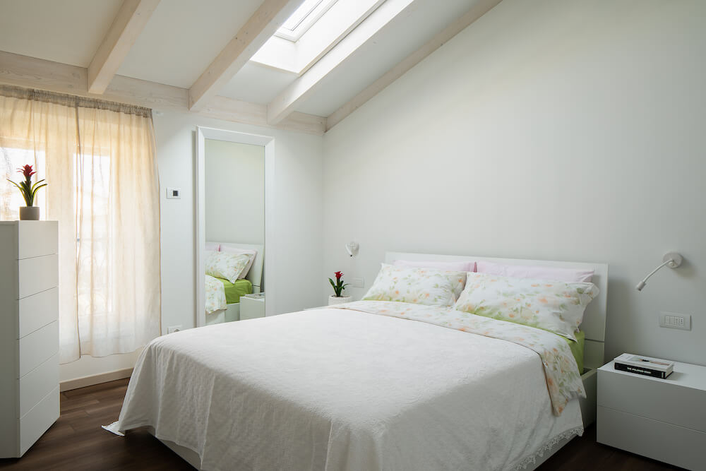 camera da letto con comodini, specchio, cassettiera, finestra sul soffitto