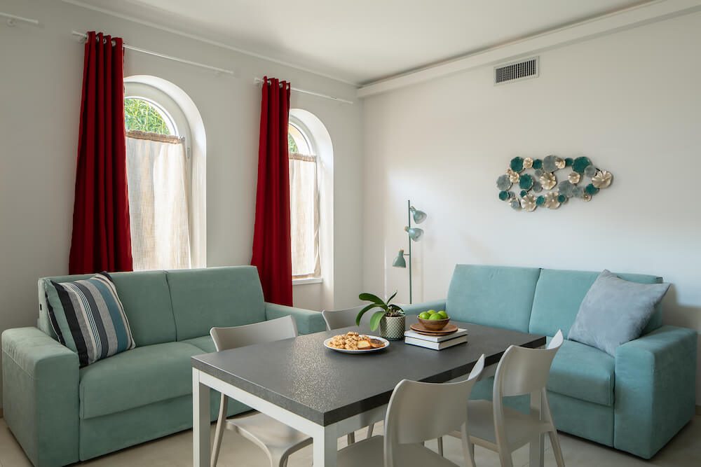 soggiorno con divani azzurri, tende rosse, finestre ad arco, tavolo e sedie ed elementi decorativi