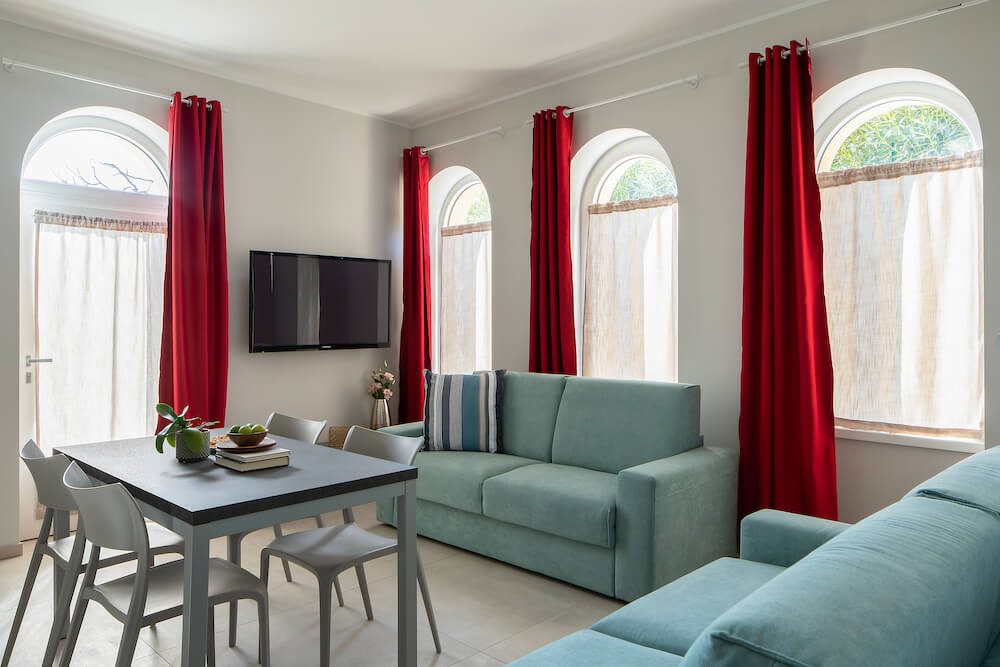 soggiorno con tv, divani azzurri, tavolo con sedie, finestre ad arco con tende rosse ed elementi decorativi