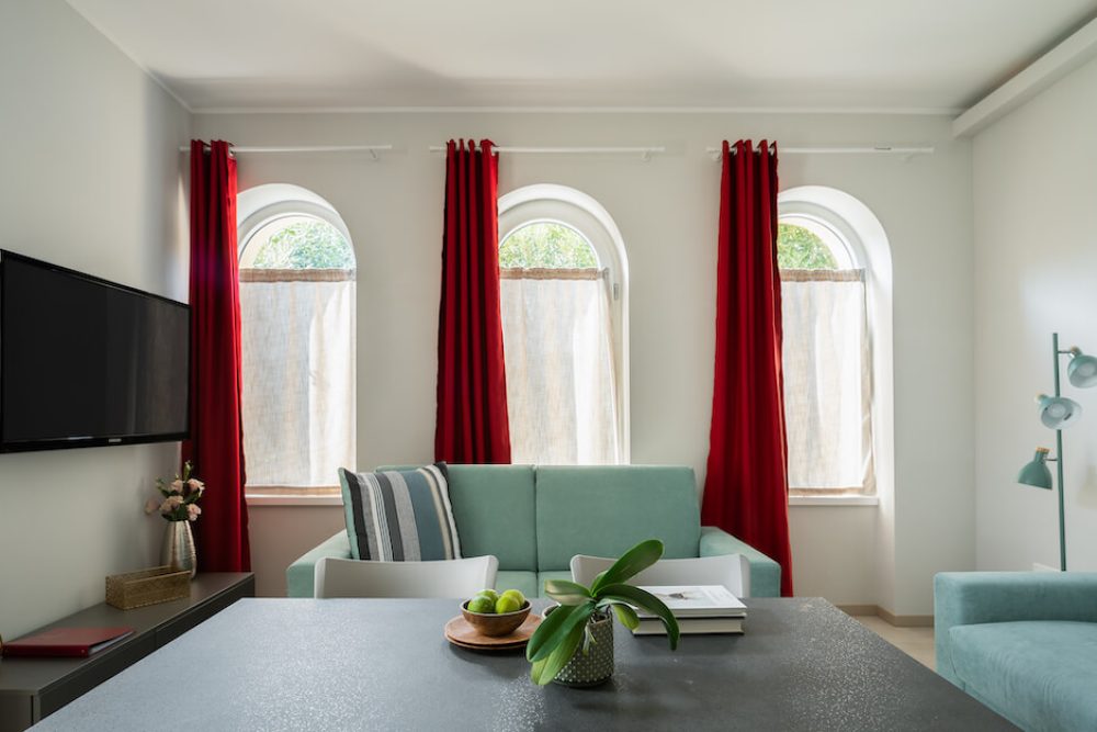 soggiorno con tv, divani azzurri, finestre ad arco con tende rosse, tavolo con elementi decorativi