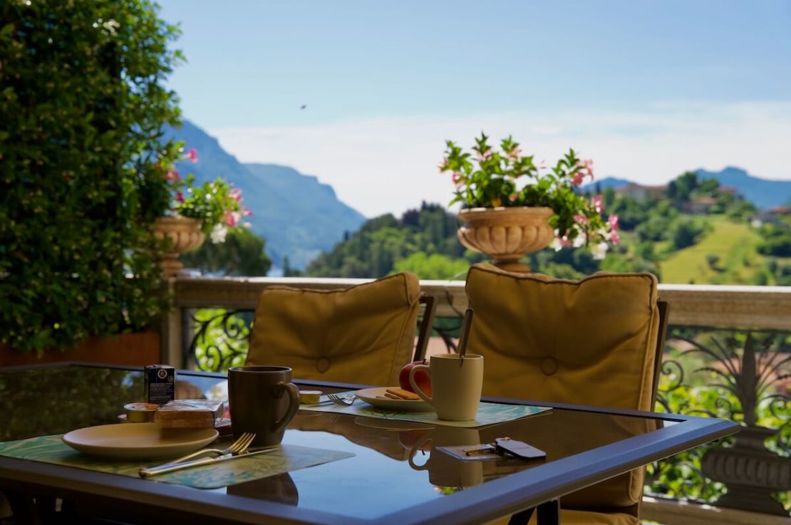 tavolo con tazze e piattini, sedie con cuscino, vasi di fiori e vista panoramica sulle colline